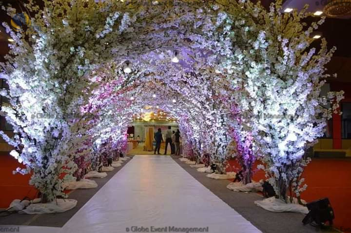 Professionally organized corporate seminar with stage and seating arrangements. Stylish product launch event setup with lights and branded backdrops. Corporate gala dinner with elegant table decor and ambient lighting. Annual day event with large LED screens and stunning stage setup. Beautifully arranged outdoor seating for a private party event. Event management team setting up a large stage for a gala night. Stunning decor featuring floral arches and chandeliers for an event. Table setup with elegant glassware and centerpiece for a formal event. Stunning flower decoration for a grand wedding entrance. Outdoor event lighting with string lights and lanterns creating a magical ambiance. Creative flower arrangement for a corporate event stage. Romantic candlelight decor with floral centerpieces for a party. Wedding Planners in Bangalore