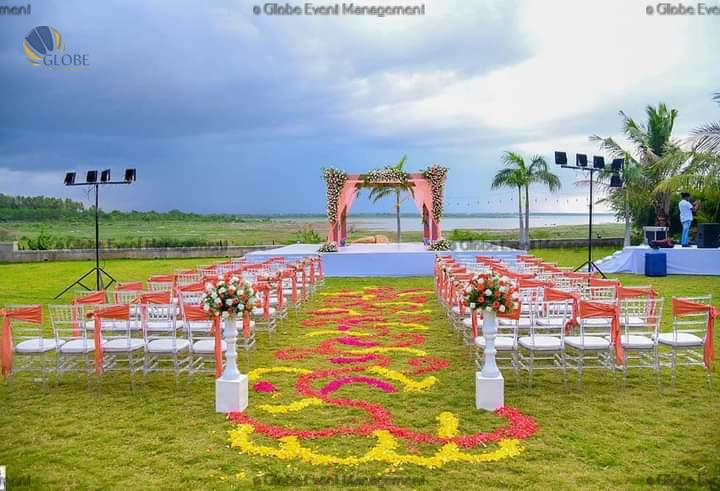 Professionally organized corporate seminar with stage and seating arrangements. Stylish product launch event setup with lights and branded backdrops. Corporate gala dinner with elegant table decor and ambient lighting. Annual day event with large LED screens and stunning stage setup. Beautifully arranged outdoor seating for a private party event. Event management team setting up a large stage for a gala night. Stunning decor featuring floral arches and chandeliers for an event. Table setup with elegant glassware and centerpiece for a formal event. Stunning flower decoration for a grand wedding entrance. Outdoor event lighting with string lights and lanterns creating a magical ambiance. Creative flower arrangement for a corporate event stage. Romantic candlelight decor with floral centerpieces for a party. Wedding Planners in Bangalore