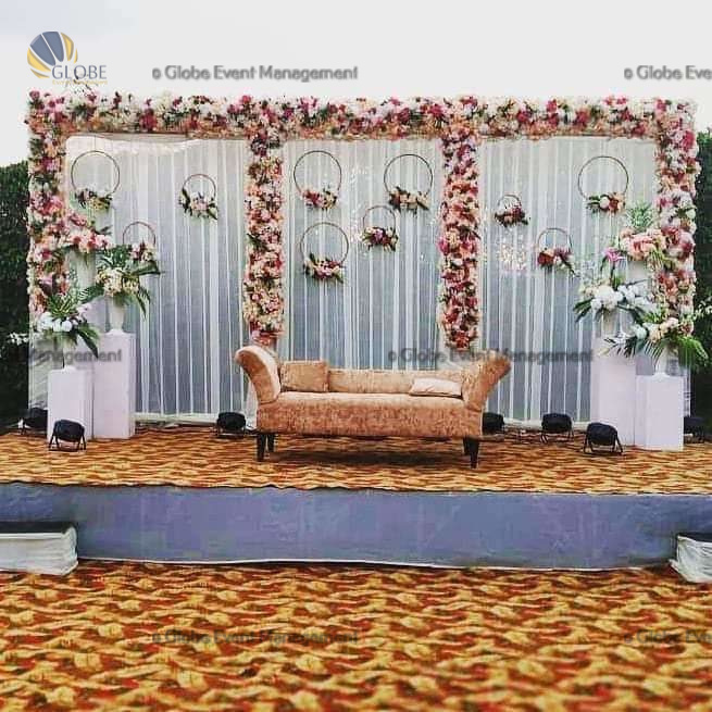 Professionally organized corporate seminar with stage and seating arrangements. Stylish product launch event setup with lights and branded backdrops. Corporate gala dinner with elegant table decor and ambient lighting. Annual day event with large LED screens and stunning stage setup. Beautifully arranged outdoor seating for a private party event. Event management team setting up a large stage for a gala night. Stunning decor featuring floral arches and chandeliers for an event. Table setup with elegant glassware and centerpiece for a formal event. Stunning flower decoration for a grand wedding entrance. Outdoor event lighting with string lights and lanterns creating a magical ambiance. Creative flower arrangement for a corporate event stage. Romantic candlelight decor with floral centerpieces for a party.