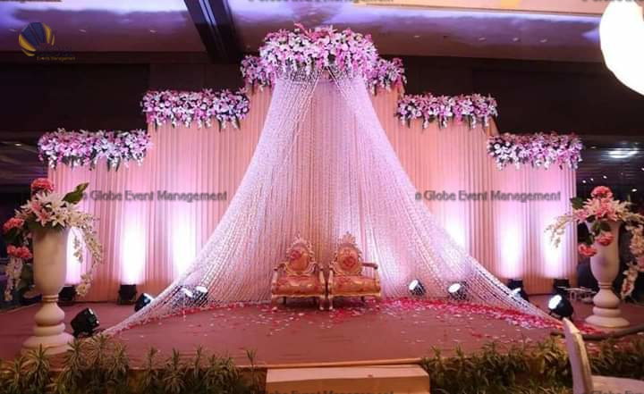 Professionally organized corporate seminar with stage and seating arrangements. Stylish product launch event setup with lights and branded backdrops. Corporate gala dinner with elegant table decor and ambient lighting. Annual day event with large LED screens and stunning stage setup. Beautifully arranged outdoor seating for a private party event. Event management team setting up a large stage for a gala night. Stunning decor featuring floral arches and chandeliers for an event. Table setup with elegant glassware and centerpiece for a formal event. Stunning flower decoration for a grand wedding entrance. Outdoor event lighting with string lights and lanterns creating a magical ambiance. Creative flower arrangement for a corporate event stage. Romantic candlelight decor with floral centerpieces for a party. Wedding Planners in Bangalore