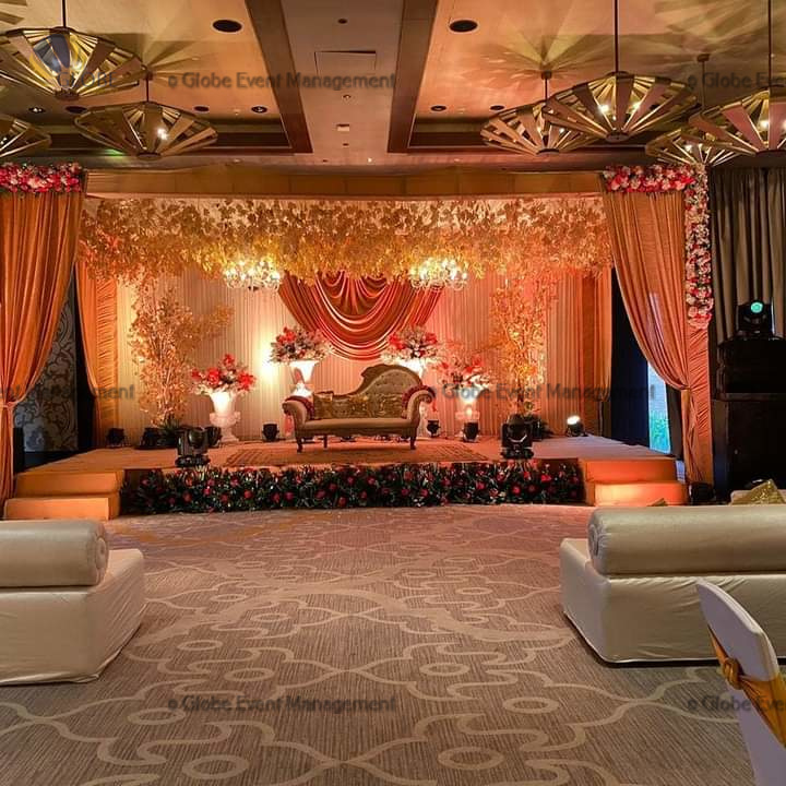 Professionally organized corporate seminar with stage and seating arrangements. Stylish product launch event setup with lights and branded backdrops. Corporate gala dinner with elegant table decor and ambient lighting. Annual day event with large LED screens and stunning stage setup. Beautifully arranged outdoor seating for a private party event. Event management team setting up a large stage for a gala night. Stunning decor featuring floral arches and chandeliers for an event. Table setup with elegant glassware and centerpiece for a formal event. Stunning flower decoration for a grand wedding entrance. Outdoor event lighting with string lights and lanterns creating a magical ambiance. Creative flower arrangement for a corporate event stage. Romantic candlelight decor with floral centerpieces for a party.